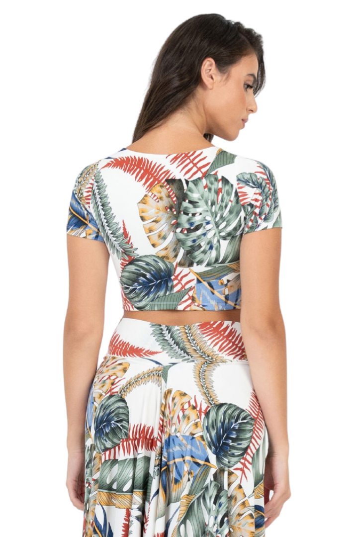 A woman shown from the back wearing a matching two-piece set with a white base and a colorful tropical leaf print in green, blue, red, and gold.