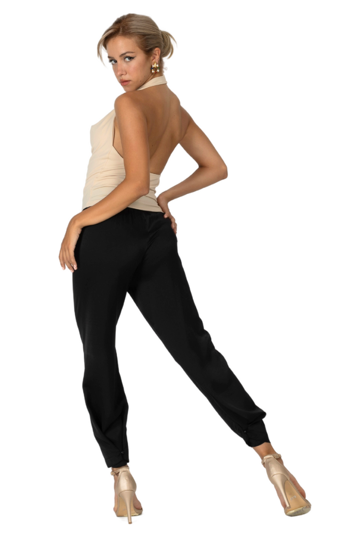 Woman wearing a beige sleeveless top and black pants on a white background