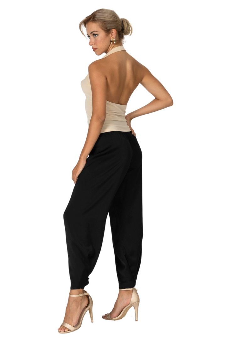 Woman wearing a beige top and black harem pants on a white background