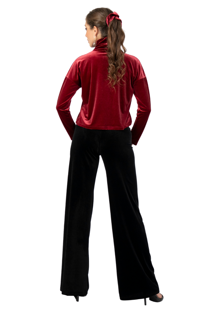 Woman wearing a red velvet top and black pants on a white background